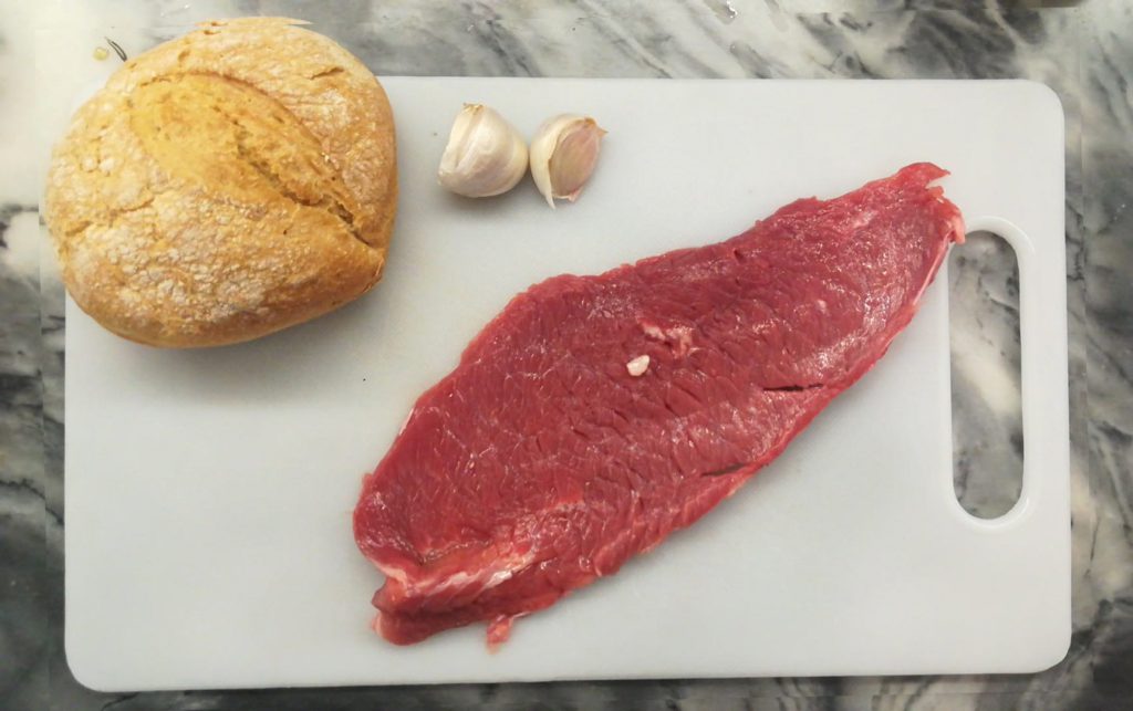 Steak, bread roll, and two cloves of garlic